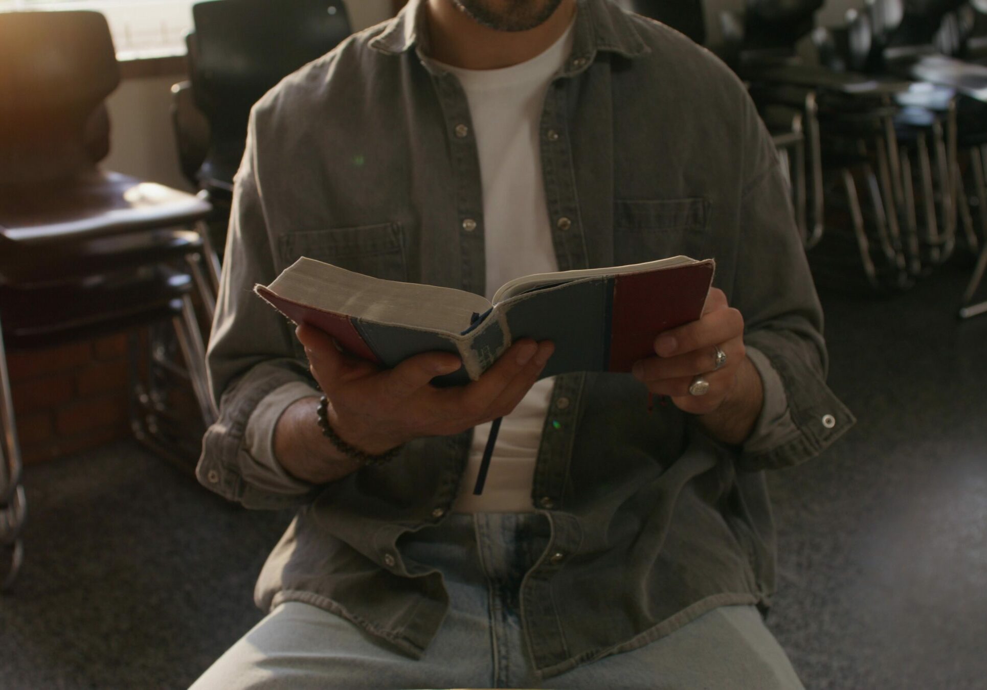 A man holds Bibles in his hands, sitting indoors, close-up of his hands, unrecognizable person. Daylight